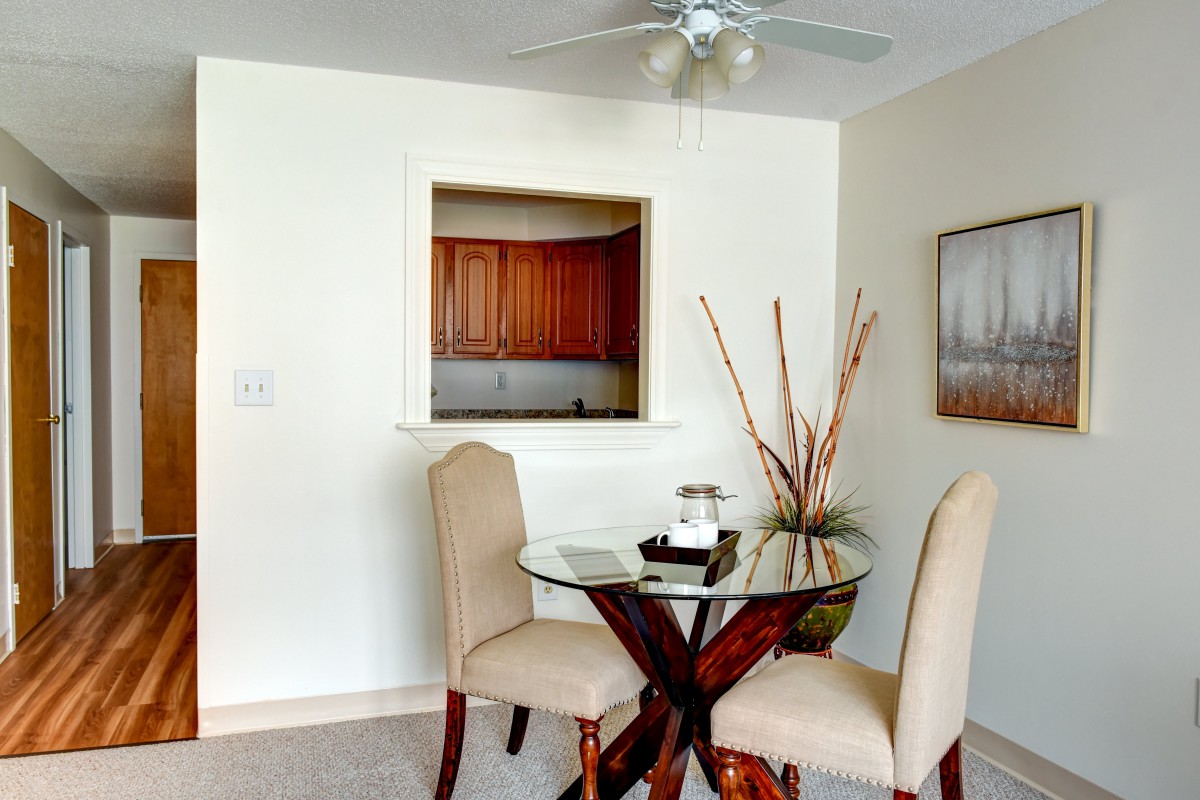 A cozy dining area with a glass table and two chairs, featuring neutral decor.