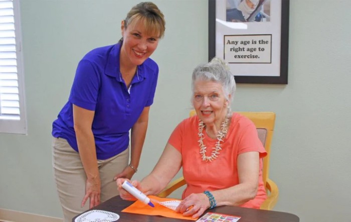 An elderly woman engaged in an activity with the assistance of a caregiver.