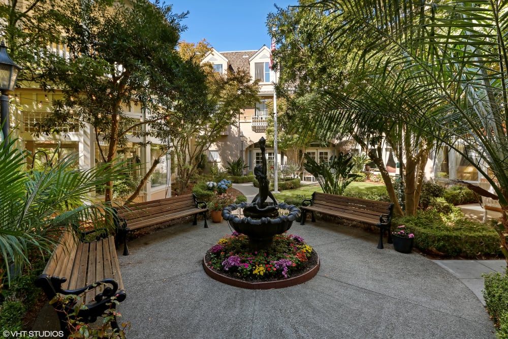 A tranquil courtyard featuring a central fountain surrounded by lush greenery and benches.