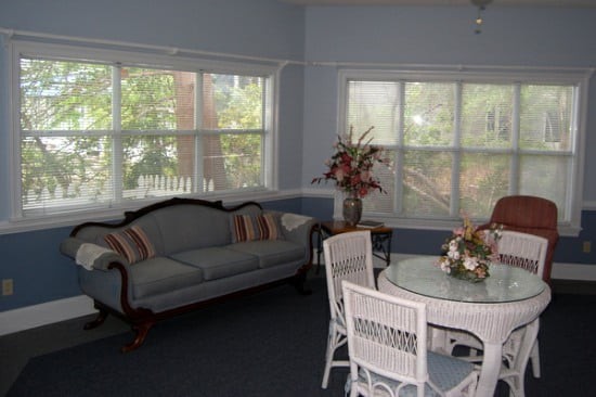 A cozy living room with a classic sofa, dining set, and large windows allowing natural light.