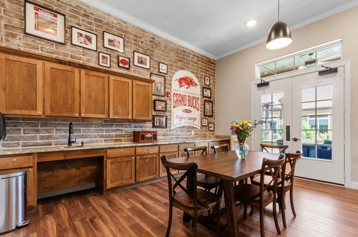 A cozy kitchen and dining area featuring wooden cabinets, a brick wall adorned with pictures, and a hardwood floor.