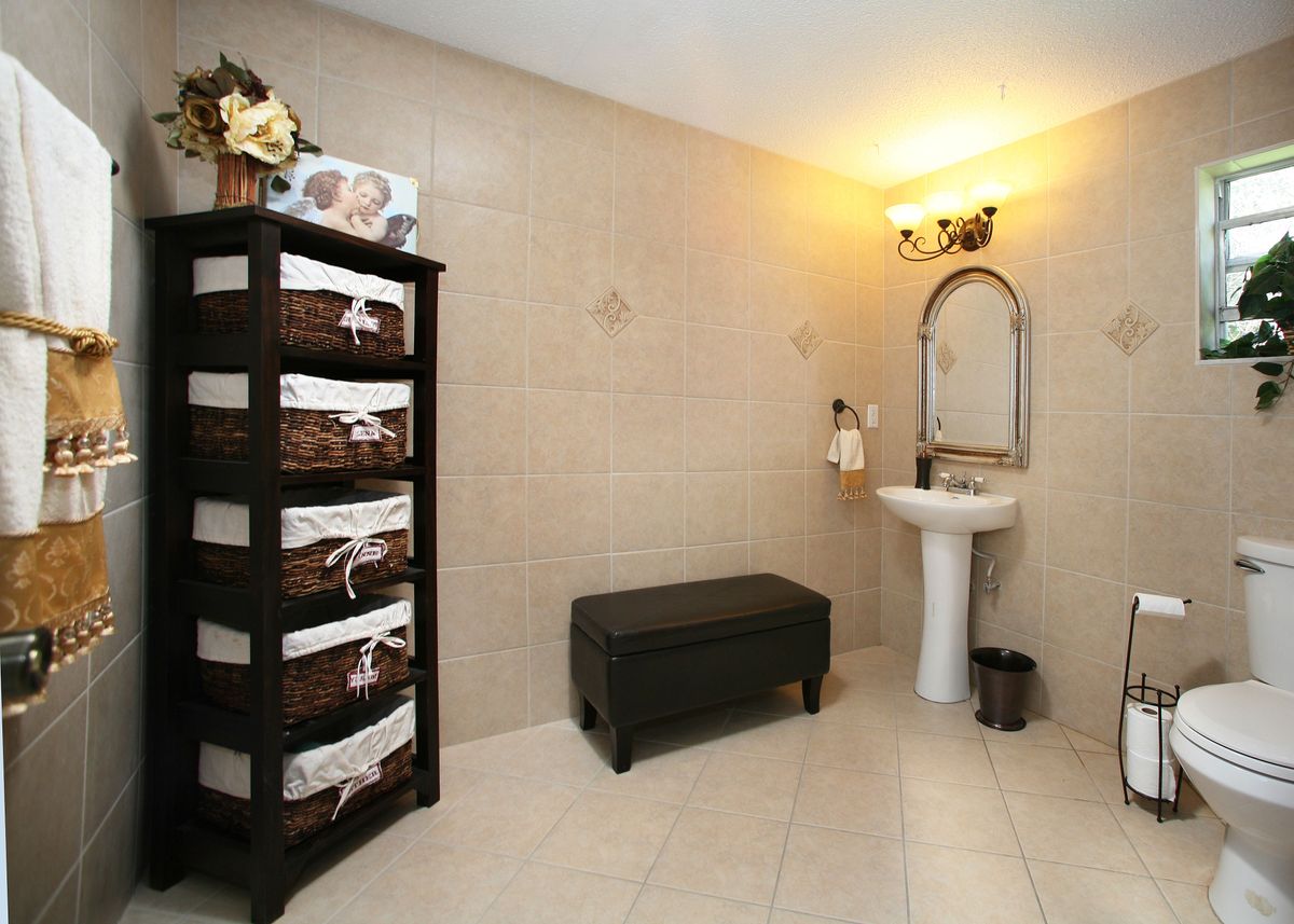 A neatly organized bathroom featuring a pedestal sink, storage baskets on shelves, and a small bench.