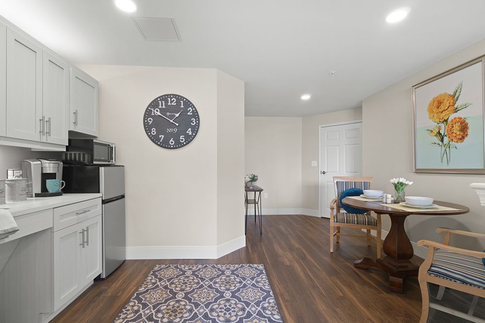 A modern kitchen interior with a wall clock, wooden flooring, and a dining table.