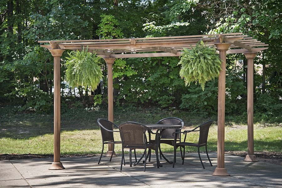 An outdoor patio with a wooden pergola, featuring a table and chairs surrounded by greenery.