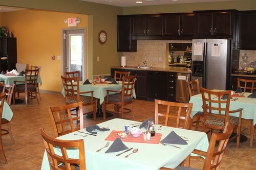A cozy dining area with neatly set tables and chairs, adjacent to a kitchen.
