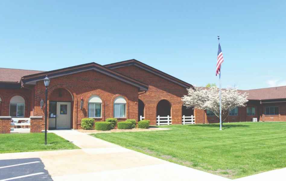 A brick building with an American flag, surrounded by a well-maintained lawn and blossoming tree.