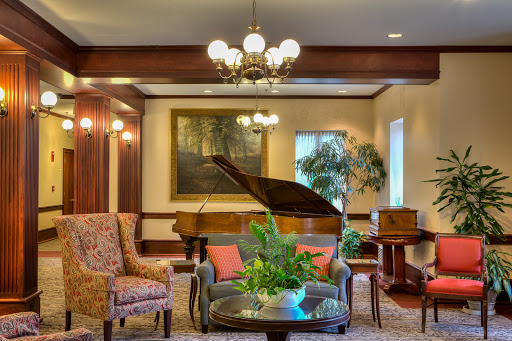 A cozy and elegant lounge area featuring a grand piano, stylish furniture, and decorative plants.