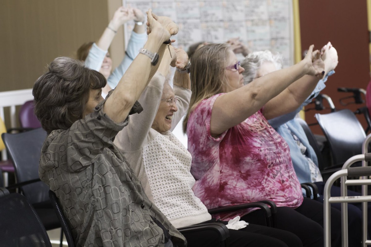A group of elderly people participating in seated exercises indoors.