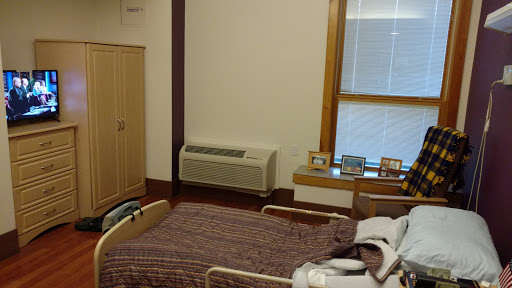 A view of a hospital room featuring a bed, an air conditioning unit, and personal photographs displayed on a ledge.
