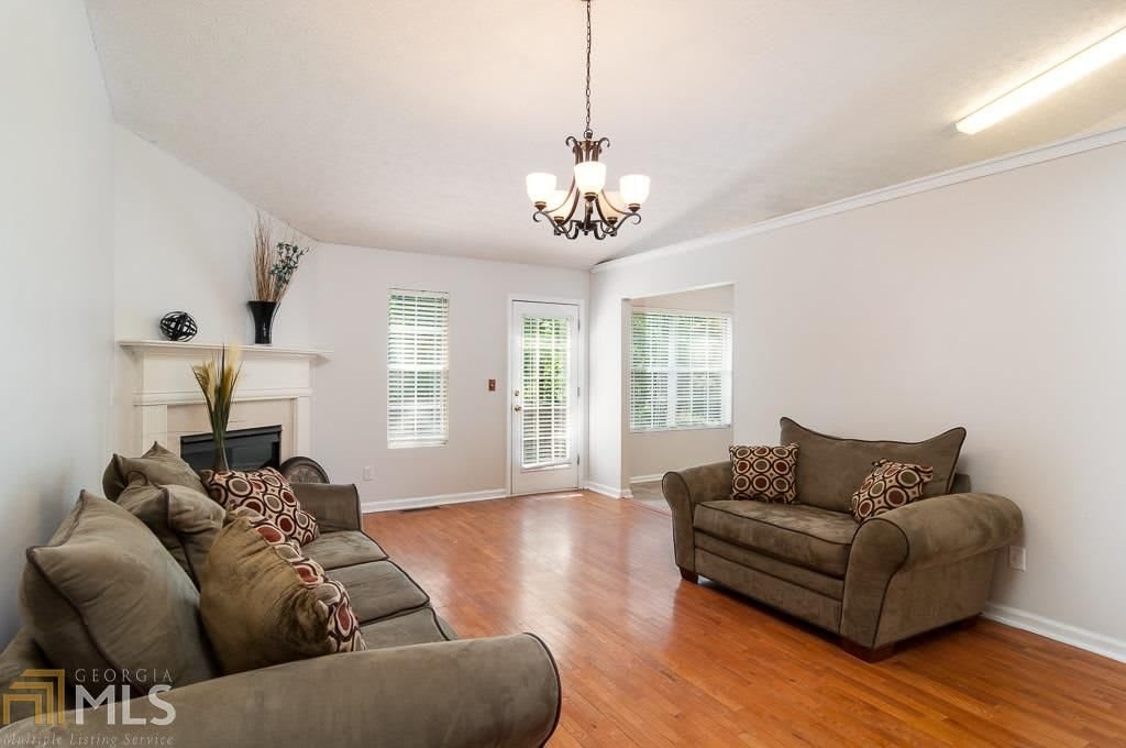 A bright and cozy living room with sofas, wooden flooring, and a chandelier.