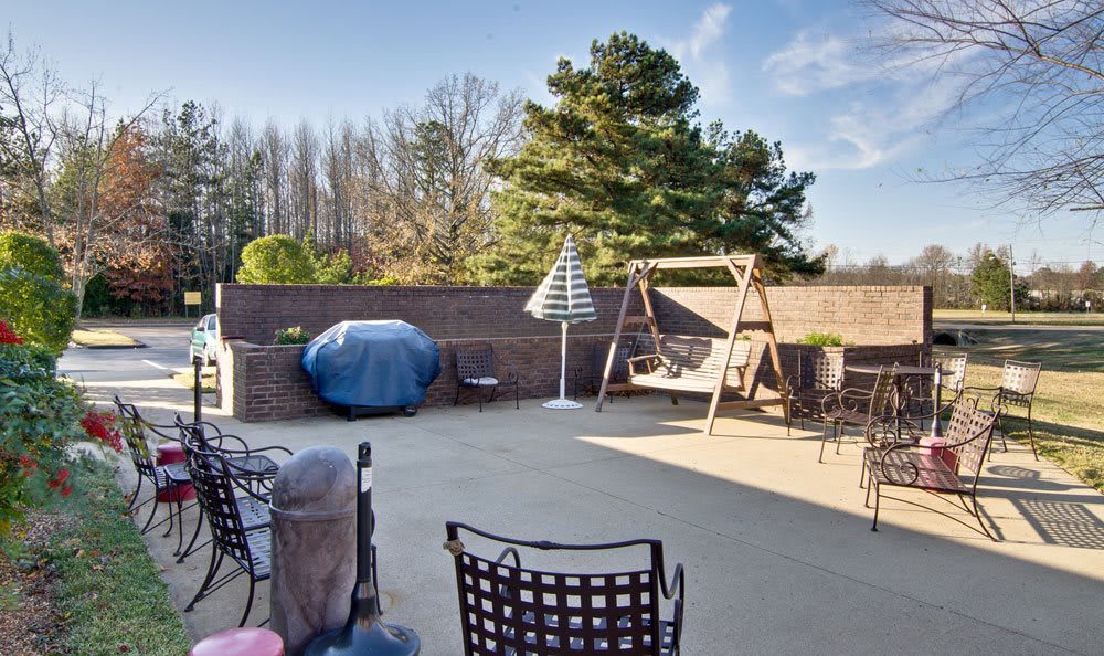 Sunny patio with outdoor furniture, a swing, and a grill surrounded by trees.