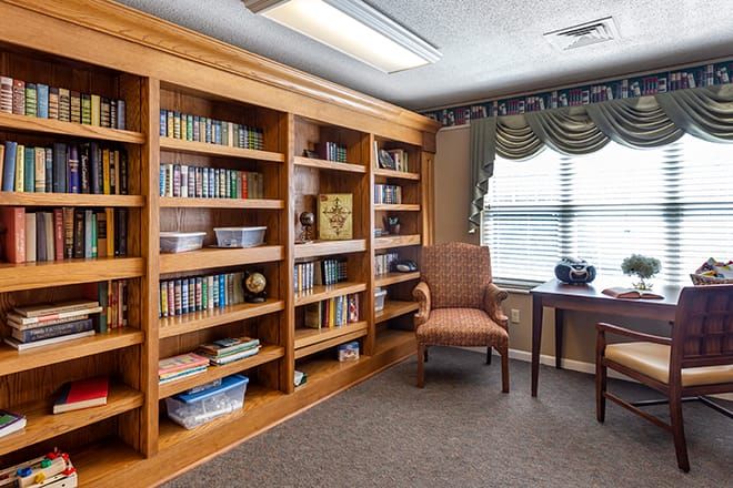 A cozy reading room with a well-stocked bookshelf, an armchair, and a table near a window.