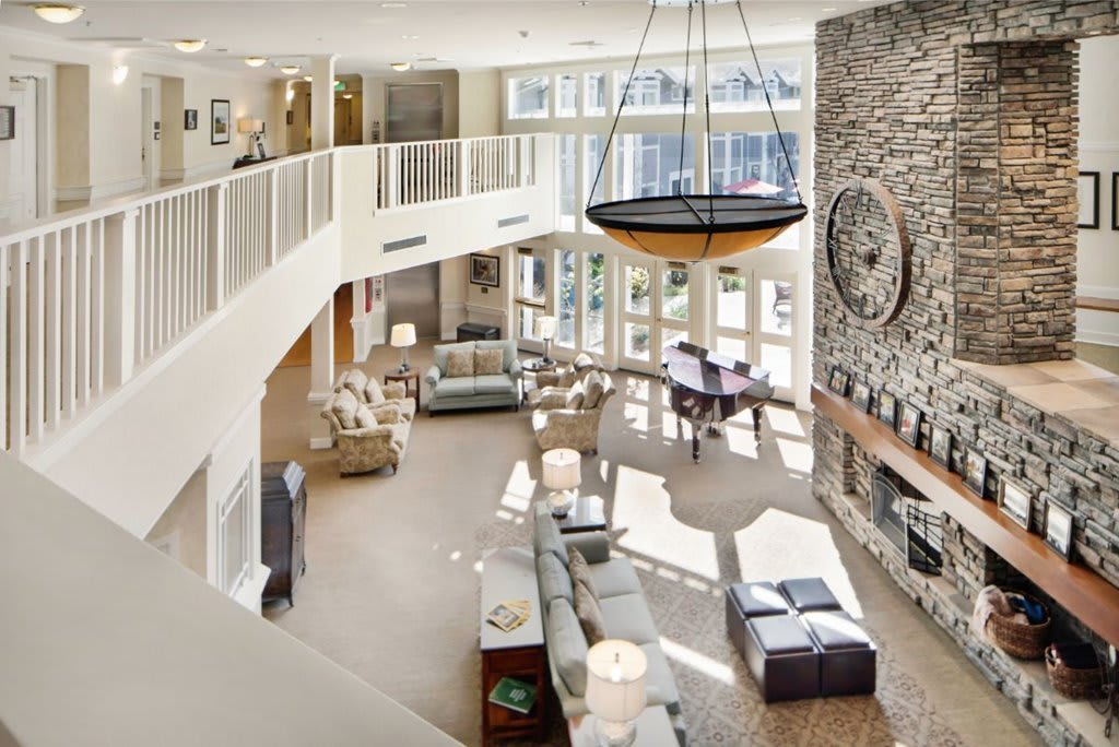 A modern, spacious living room with large windows and a stone fireplace, featuring contemporary furniture and an open two-story design.