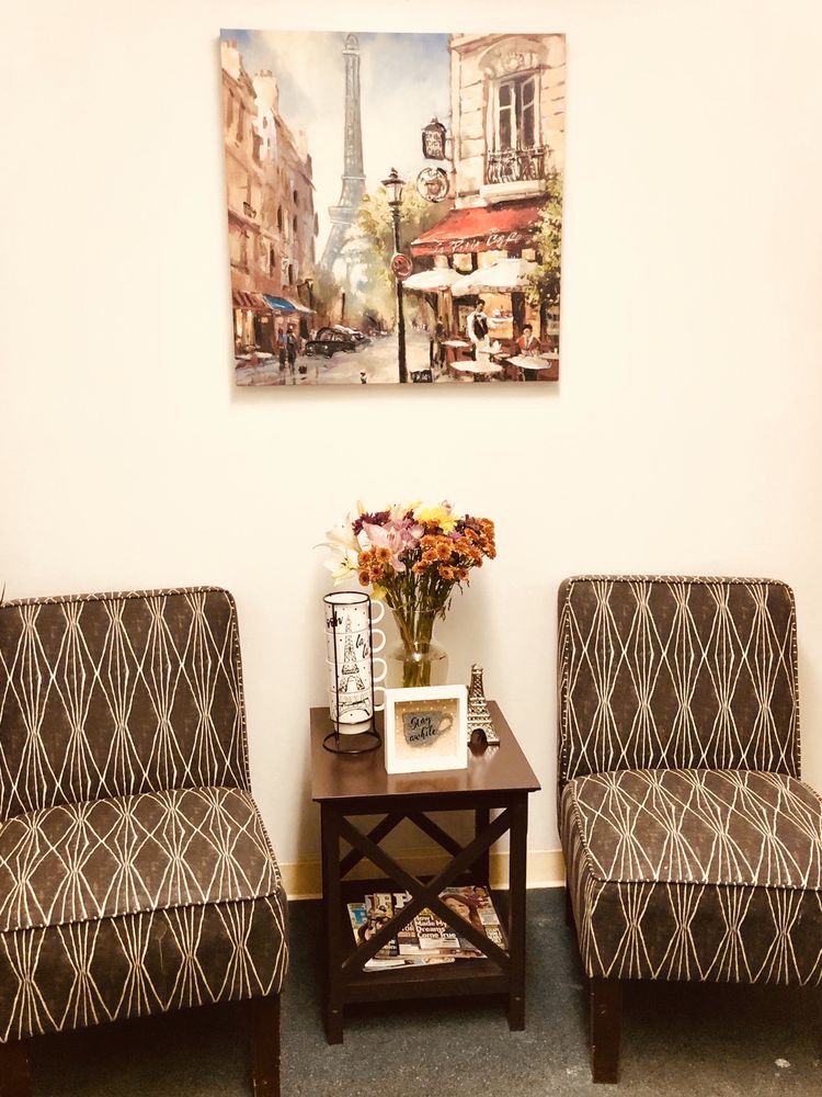 A cozy living space with patterned chairs, a small wooden table with flowers, and a Parisian-themed painting.