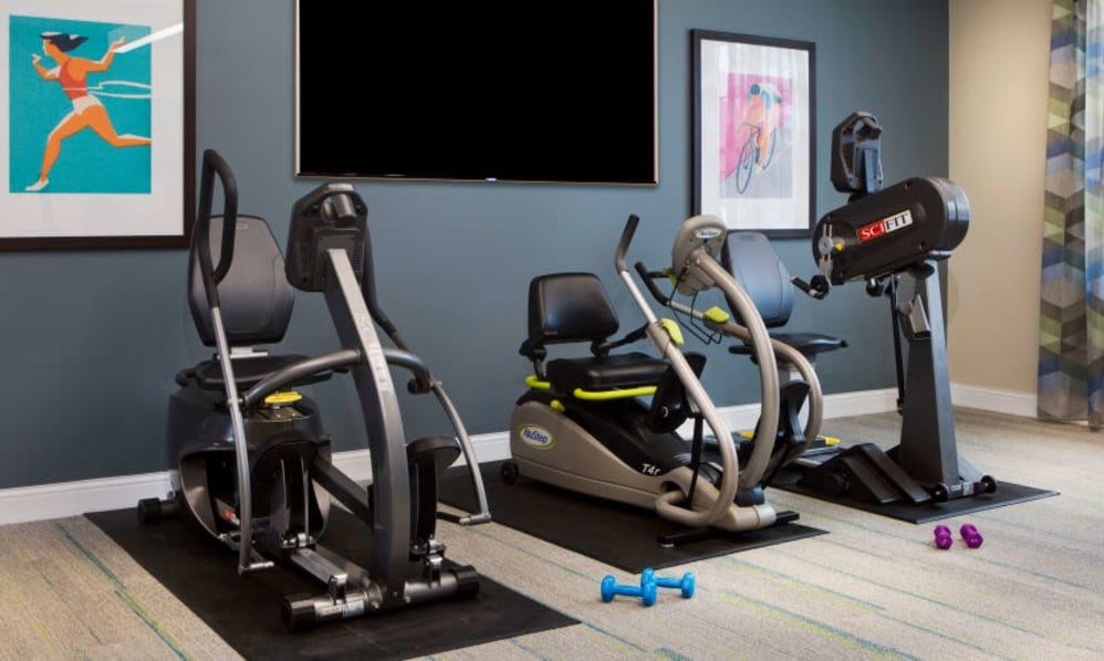 A modern gym featuring stationary bikes, a treadmill, and dumbbells.