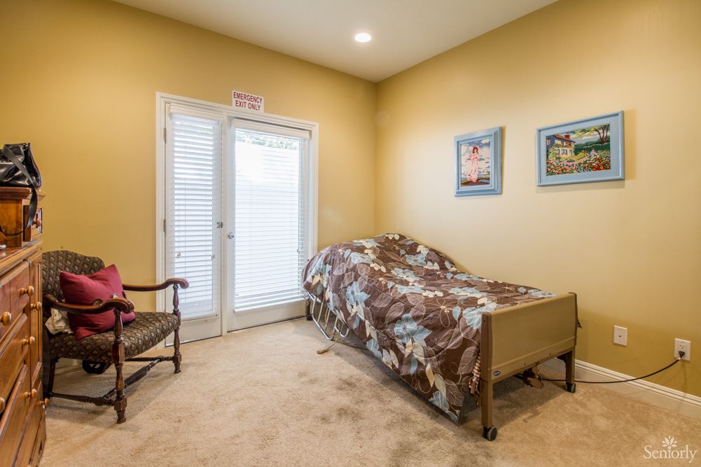 A cozy bedroom with a single bed, decorated with paintings and bathed in warm lighting.