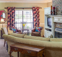 A cozy living room with a large sofa, colorful curtains, and a fireplace.