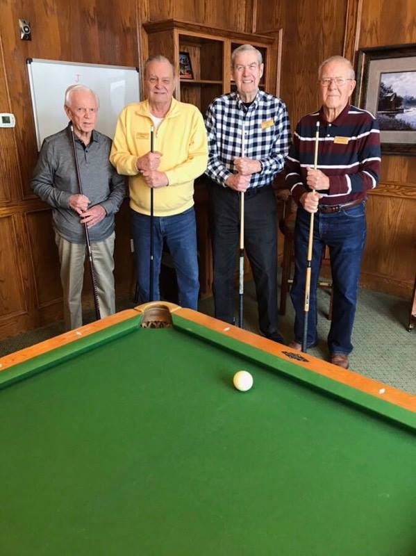 A group of four seniors standing around a pool table, each holding a cue stick.