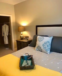A cozy bedroom with a neatly made bed, featuring decorative pillows and a bedside lamp. A robe hangs in the closet.