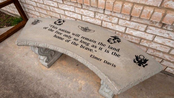 A stone bench engraved with a quote about freedom and bravery, placed against a brick wall.