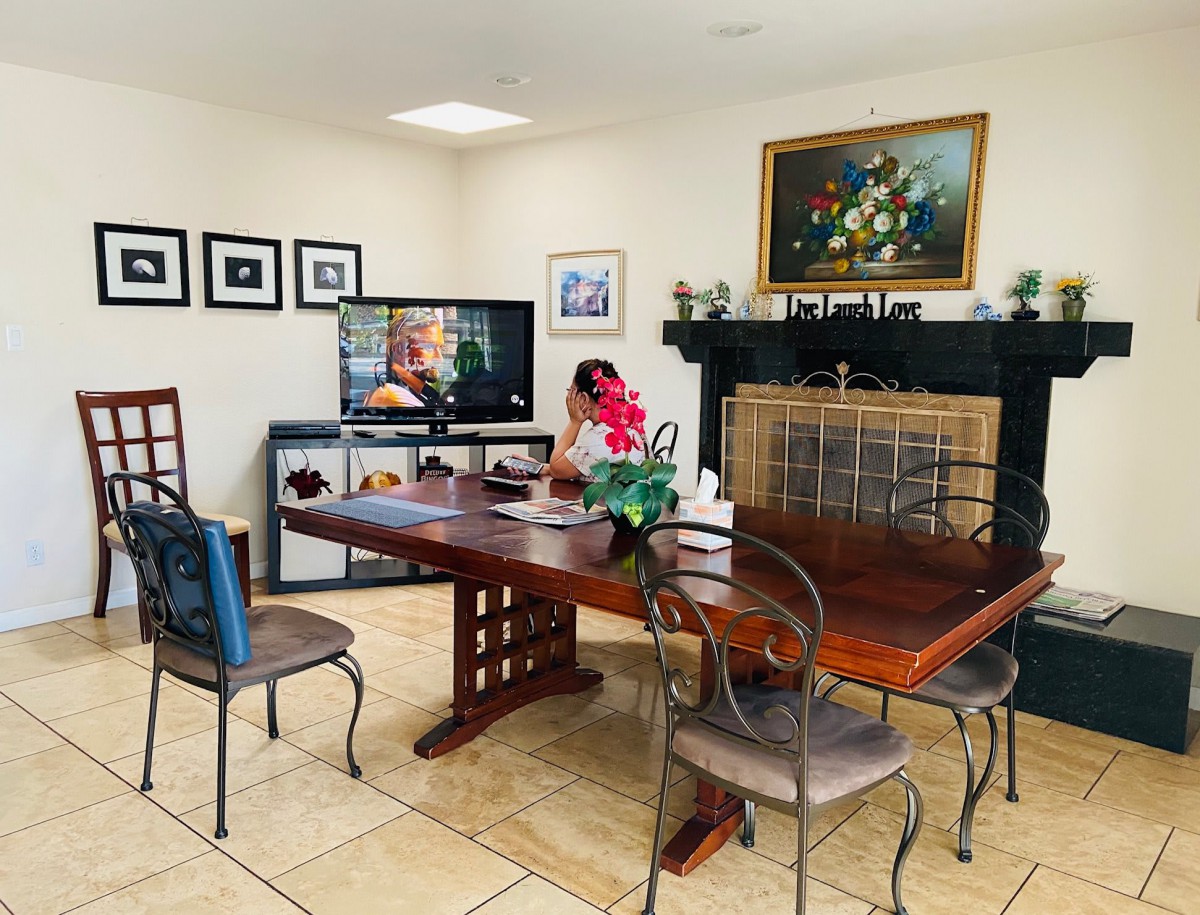 A cozy dining room with a wooden table, chairs, and a fireplace, featuring a TV and various decor elements.