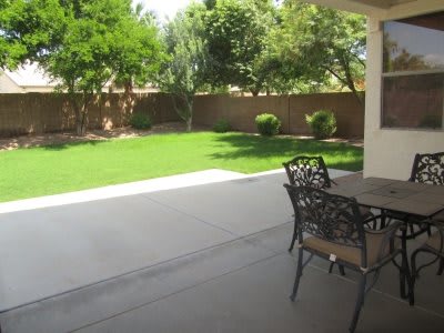 A view of a backyard with a patio, lawn, and outdoor furniture.