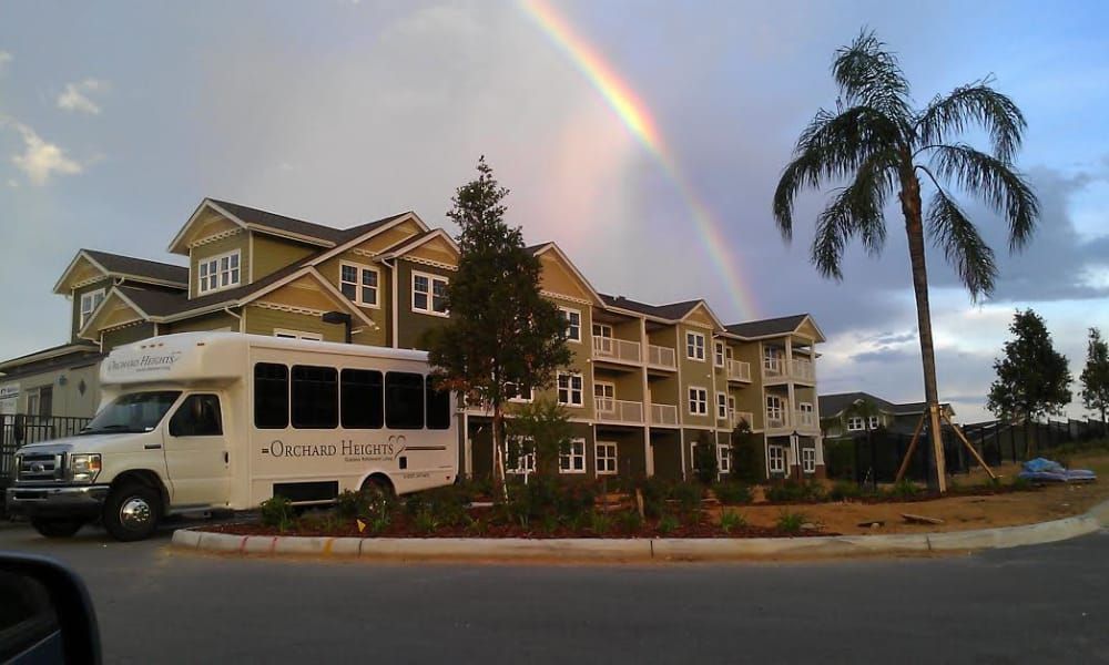 A rainbow arches over an apartment building with a bus parked in front.