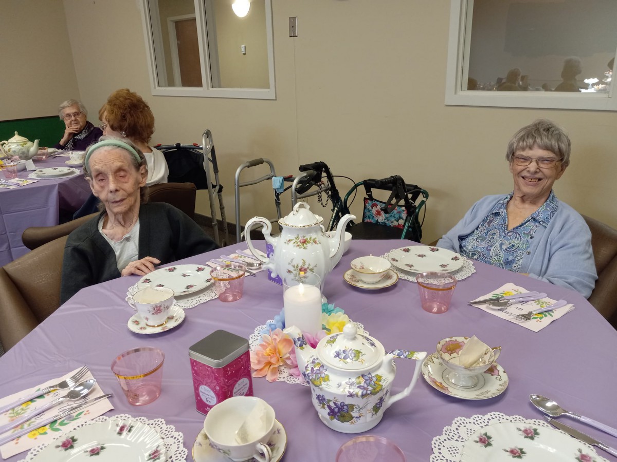A group of elderly women enjoying a tea party with a beautifully set table.