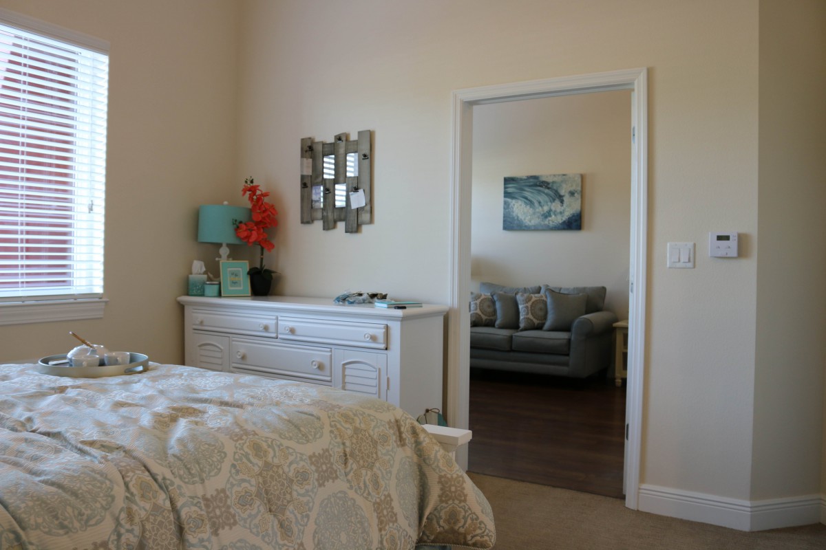 A cozy bedroom with a dresser and mirror, connected to a living space through an open doorway.
