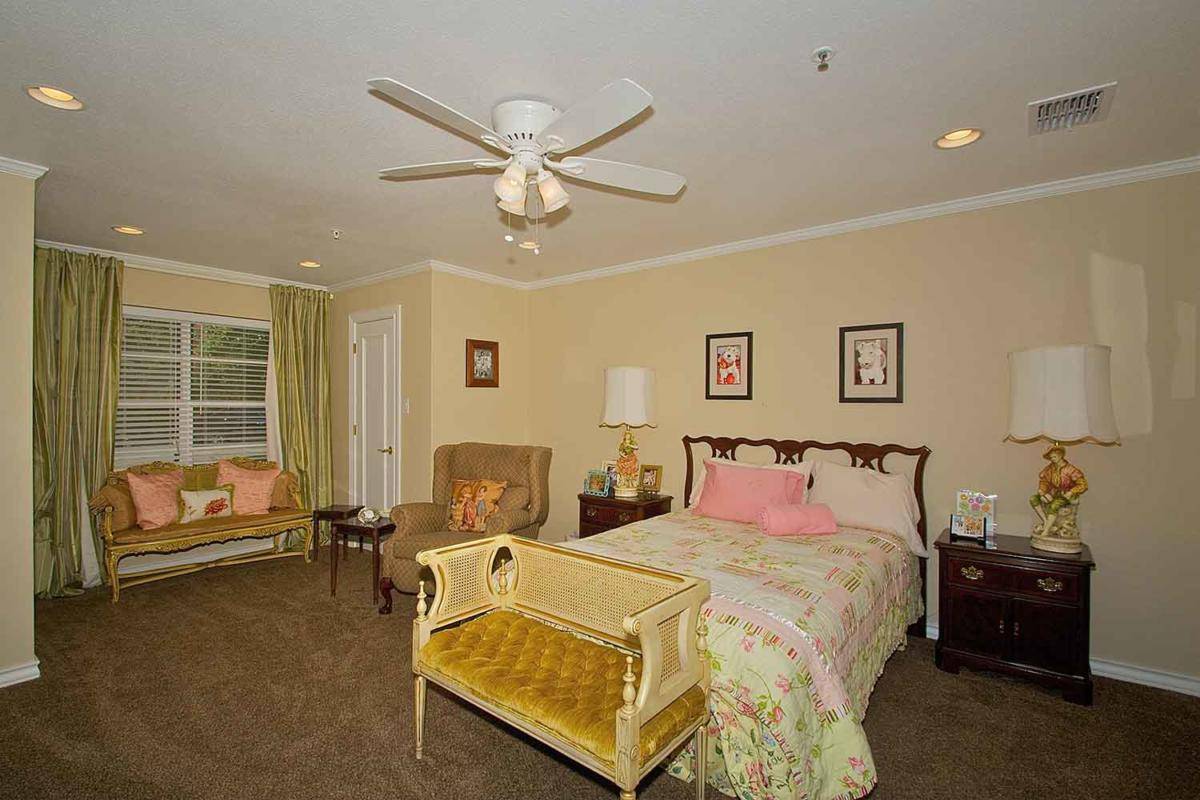 A cozy bedroom featuring a bed with decorative pillows, an armchair by the window, and a ceiling fan overhead.