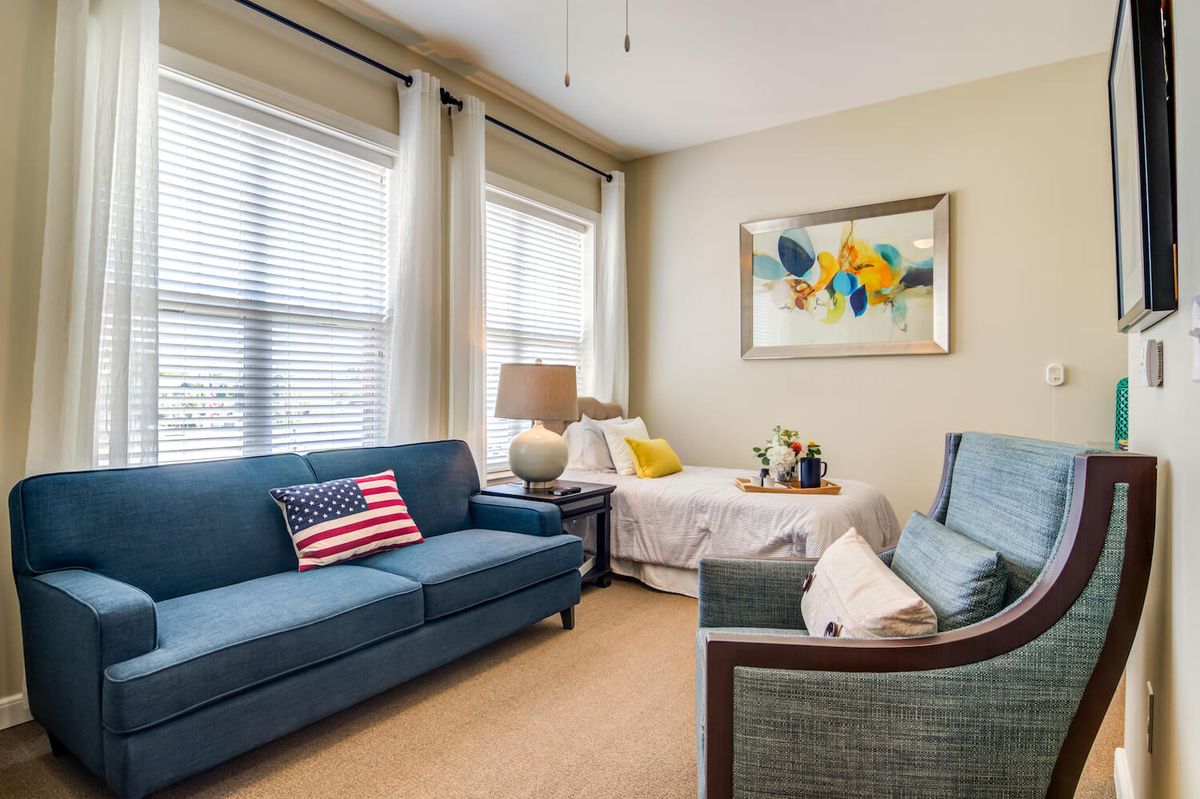 A cozy living room featuring a blue sofa with decorative pillows, including an American flag pillow, and a colorful framed artwork on the wall.
