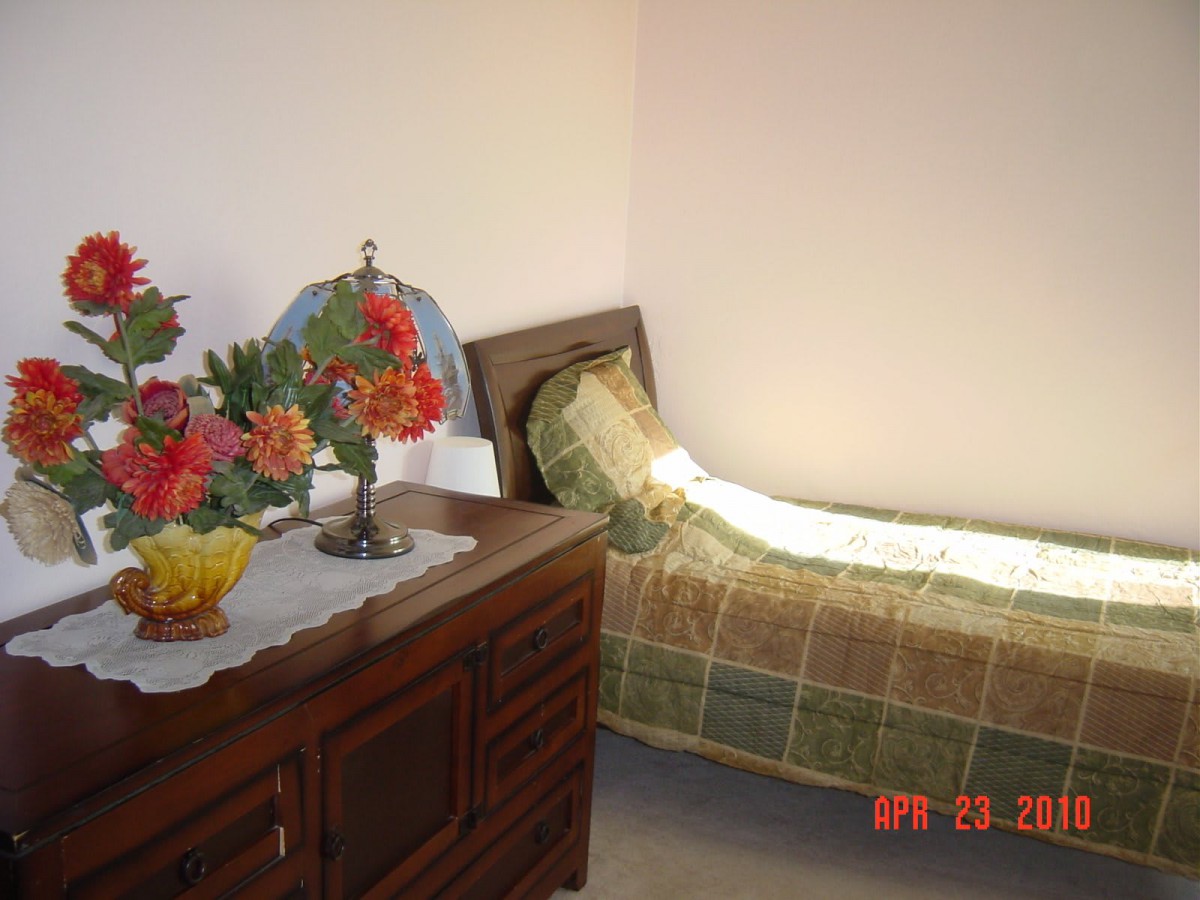 A cozy bedroom with a single bed and a dresser decorated with flowers.