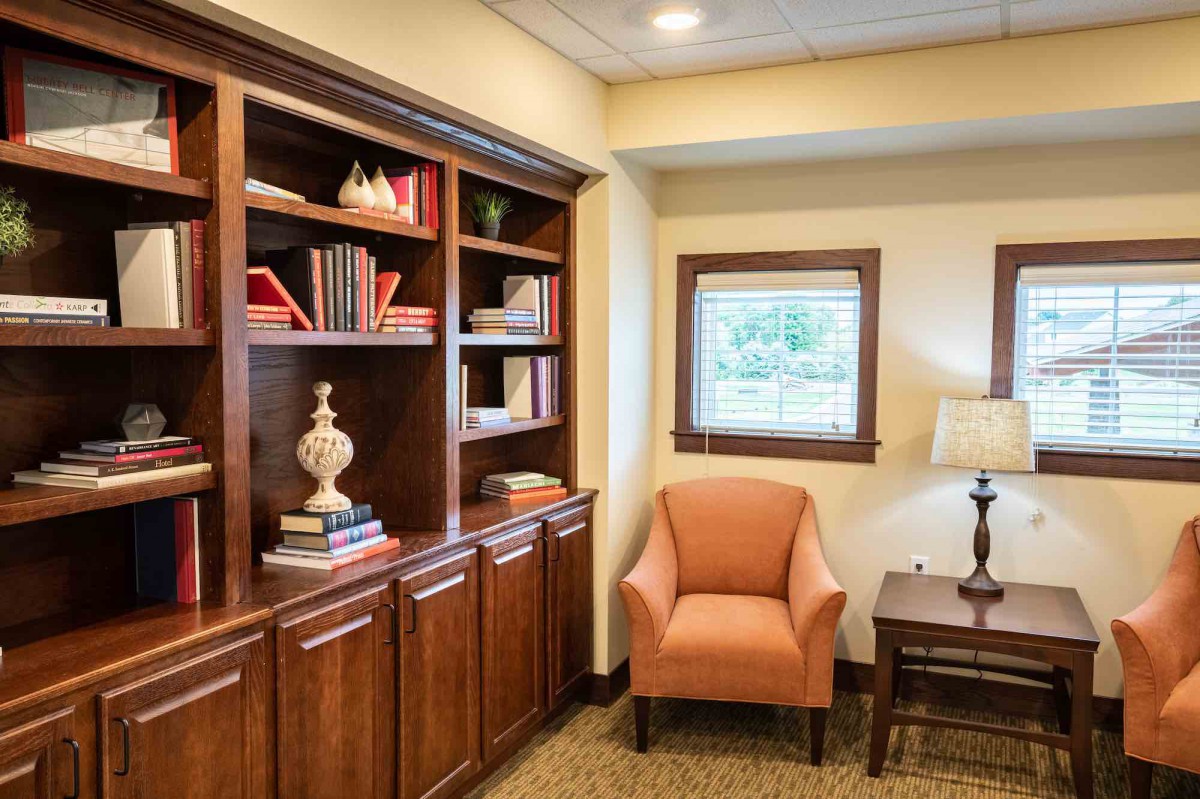 A cozy reading nook with a wooden bookshelf, comfortable armchair, and a window allowing natural light in.