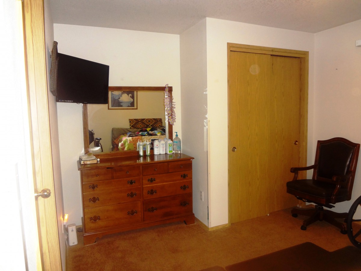 A cozy bedroom featuring a wooden dresser with a mirror, a wall-mounted television, and a closet.