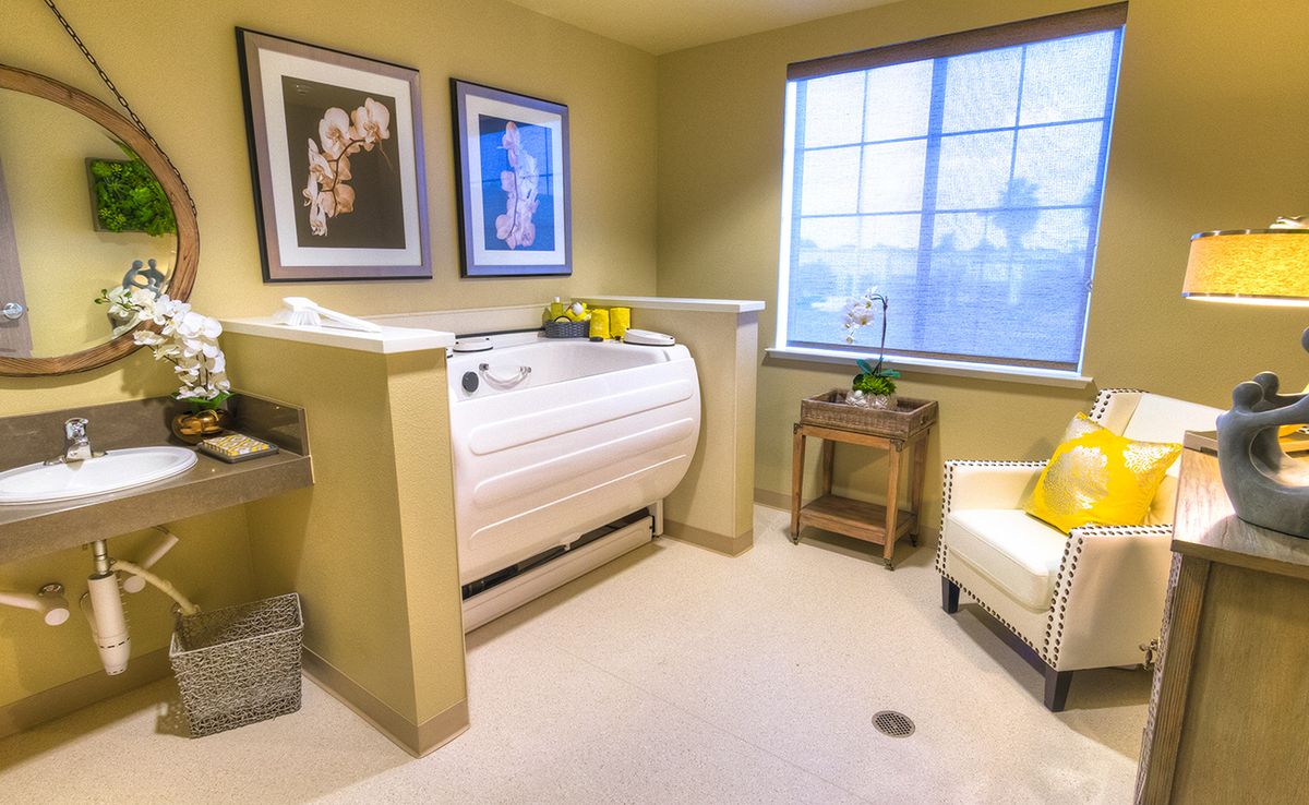 A serene spa treatment room with a modern design, featuring a massage table, comfortable chair, and calming artwork on the walls.