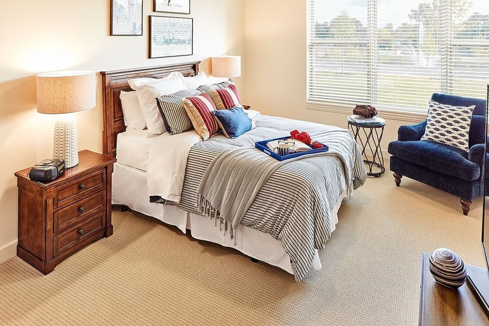 A cozy bedroom with a neatly made bed, pillows, and a bedside table with a lamp.