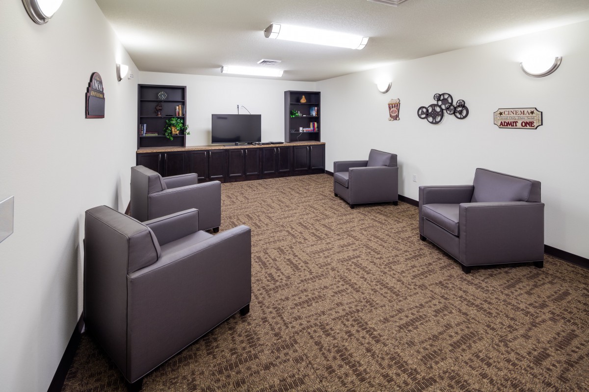 A lounge area featuring several gray armchairs, a television, and carpeted flooring.