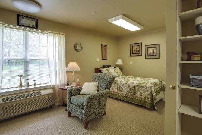 A cozy bedroom with a bed, armchair, lamp, and window with curtains.