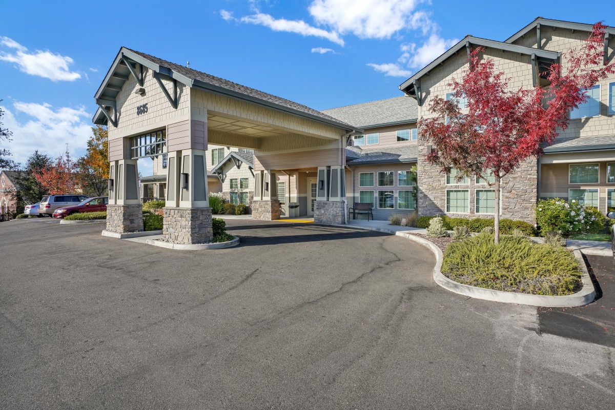 The image shows a facility with a covered entrance and well-maintained driveway, set against a clear blue sky.