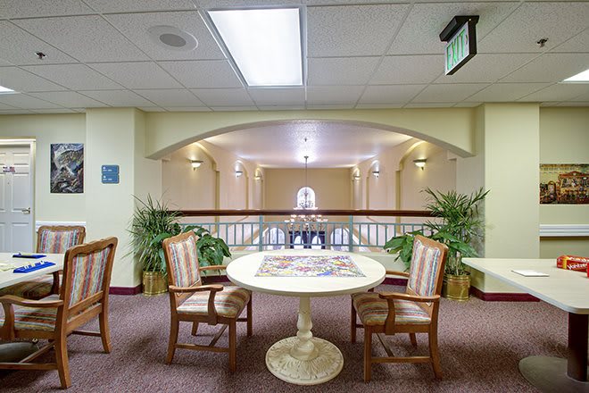 A cozy interior space with a round table and chairs, surrounded by plants in a well-lit hallway.