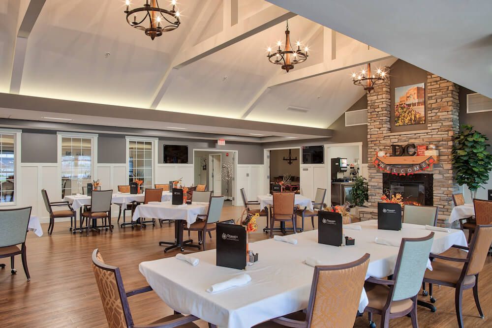 A cozy restaurant interior featuring a dining area with neatly arranged tables and chairs, chandeliers, and a fireplace.