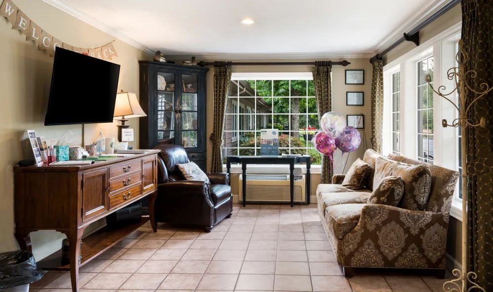 A cozy living room with a sofa, armchair, and a large window offering a garden view.