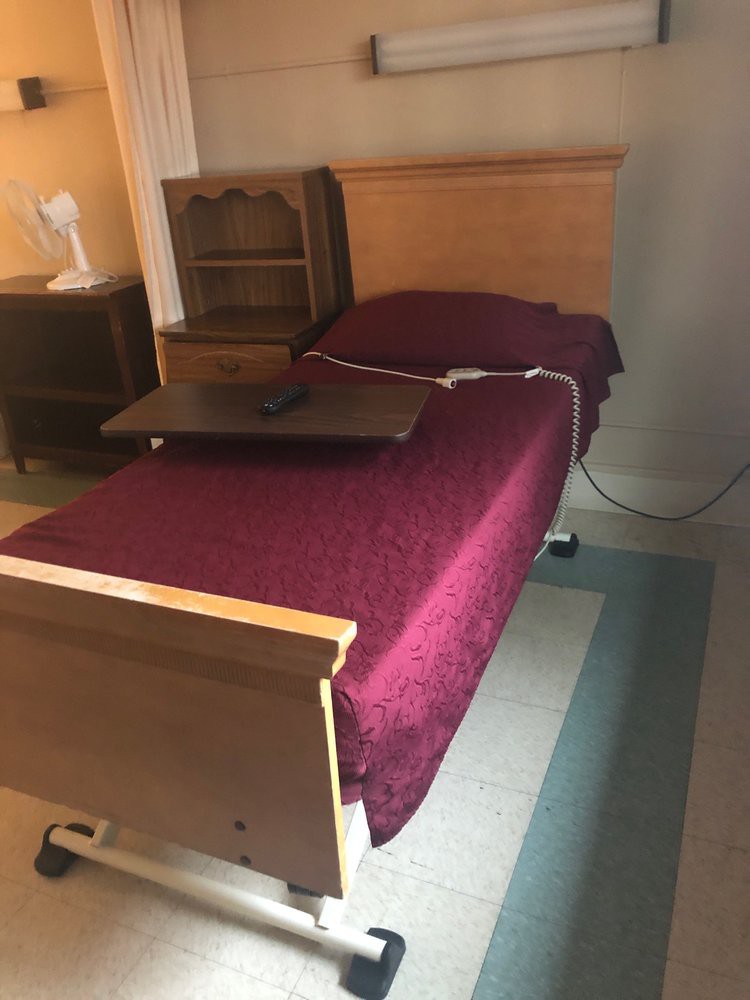 A hospital bed with a burgundy cover and an adjustable side table in a room.