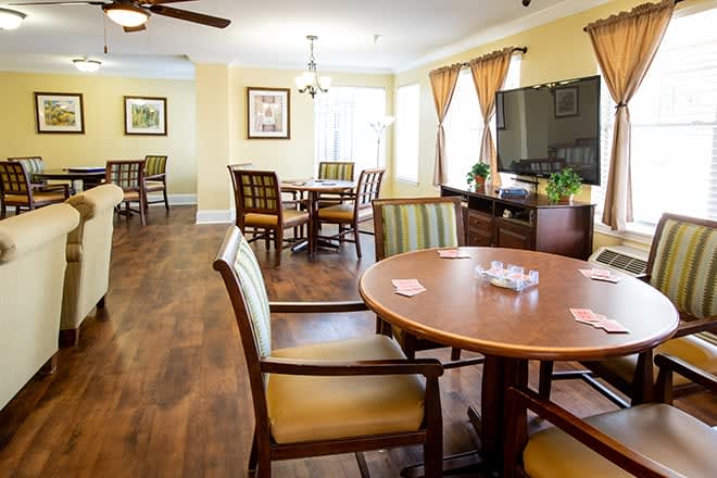 A cozy dining area with wooden tables and chairs, featuring ceiling fans and natural light from large windows.