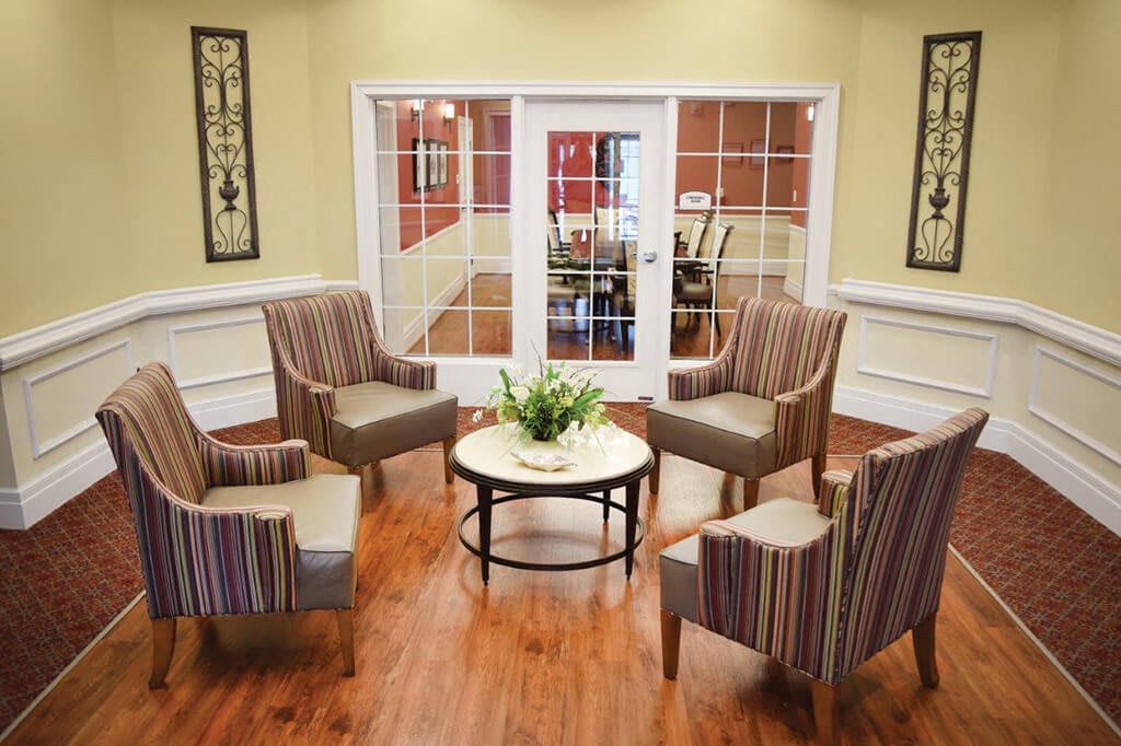 A cozy seating area with four striped chairs surrounding a round table, set on a polished wooden floor.