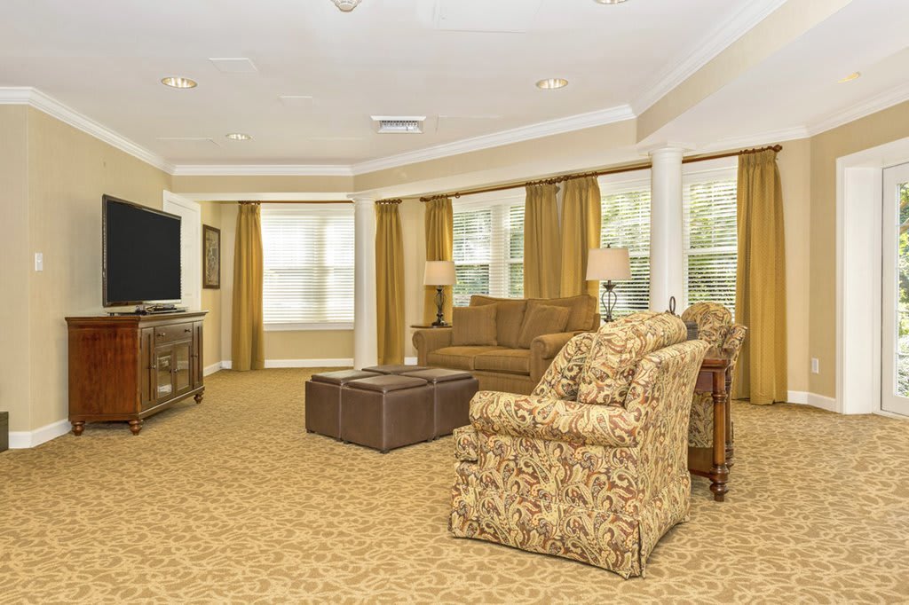 A cozy living room with patterned furniture, a large TV, and ample natural light from multiple windows.