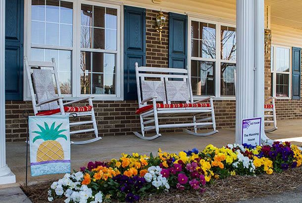 A cozy front porch with white rocking chairs and vibrant flowers.