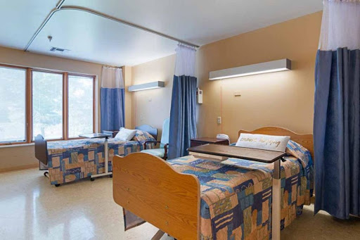 A spacious and well-lit hospital room with two beds and privacy curtains.