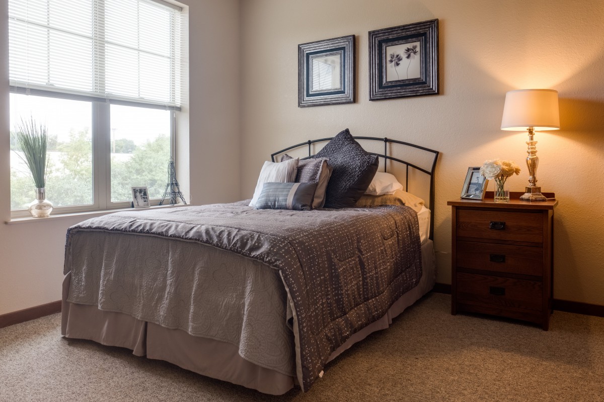 A cozy bedroom with a neatly made bed, soft lighting, and decorative framed pictures on the wall.