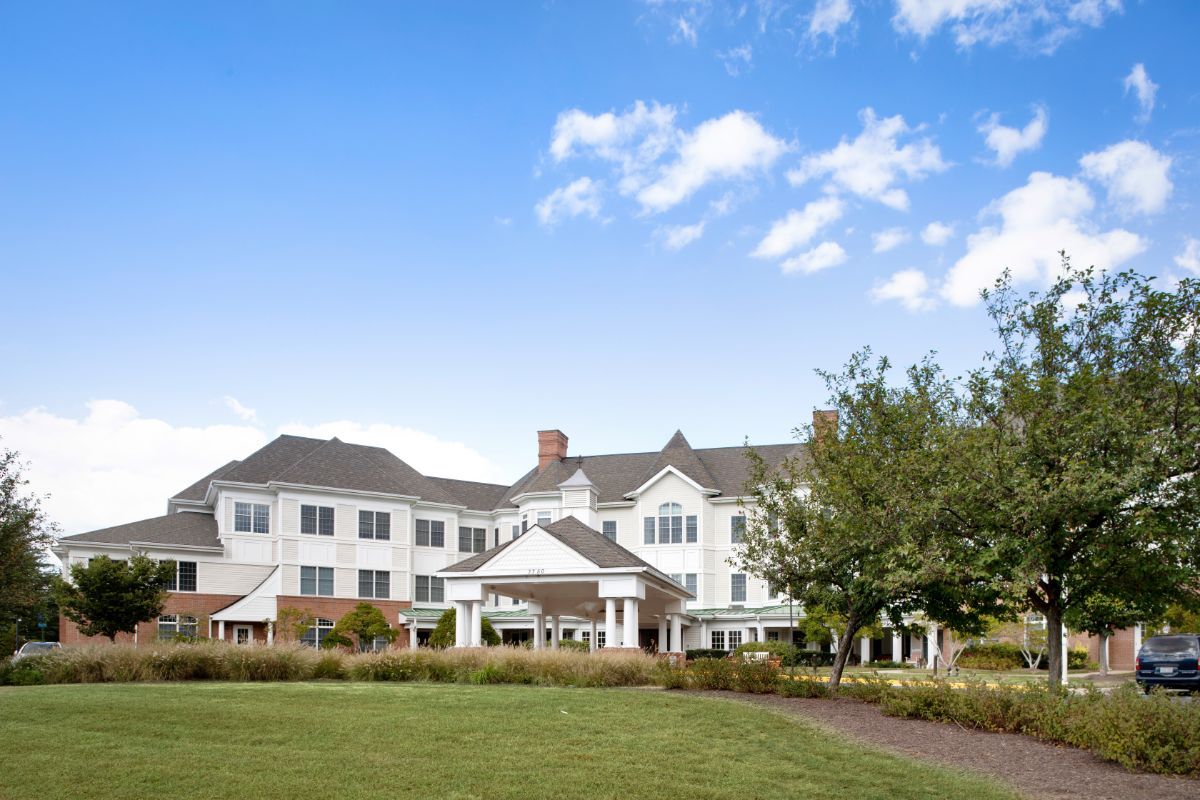 A large residential building with a landscaped front yard under a clear blue sky.